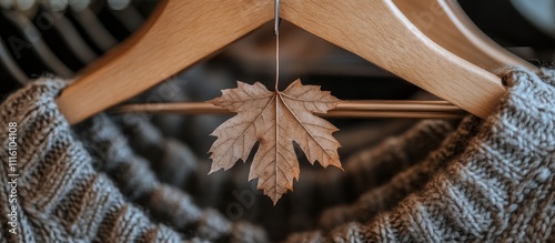 Autumn textures close up of a maple leaf hanging from a cozy chunky knit sweater on wooden hangers showcasing seasonal warmth and style photo