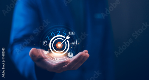Concept of future goals and strategic planning. 2025 business goal. Businessman holds a glowing digital a target with 2025 and icons for success, growth, and finance. Planning business growth.