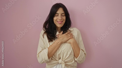 Woman smiling with hands on heart against a pink background, showcasing a joyful and appreciative mood