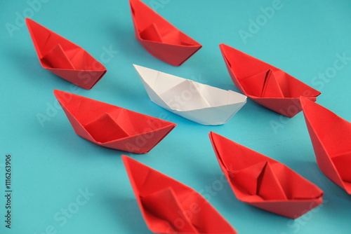 red paper ship or paper boats sailing ahead of other yellow paper ships on blue water.  flat lay with space for text. Uniqueness concept. success, leadership concept photo