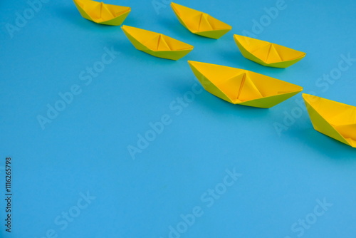 yellow paper ship or paper boats sailing ahead of other ships on blue water.  flat lay with space for text. success, leadership concept