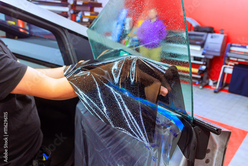 Technician worker applies window tint toa car door, ensuring an even finish while clients wait in background. photo