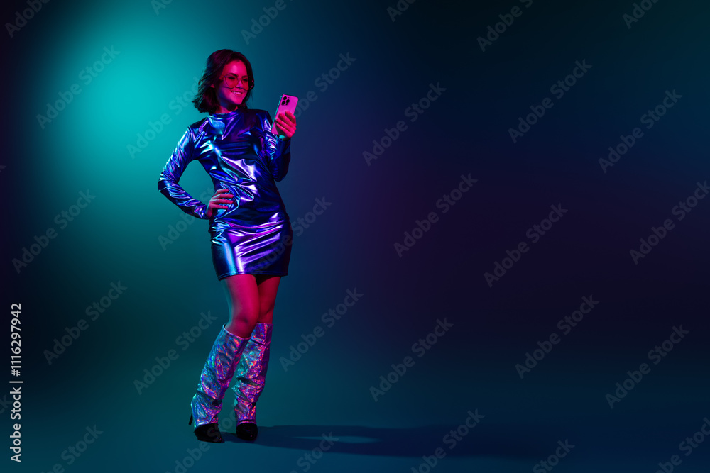 Obraz premium Full body portrait of stunning young woman hold phone empty space wear shiny dress neon light dark blue background