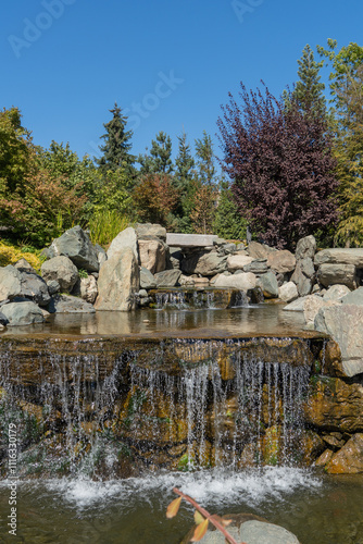 Water falls from height of 7 meters into artificial rocky riverbed. Close-up. Triple waterfall in Japanese Garden. Riverbed is divided into three streams, which turn into waterfalls.