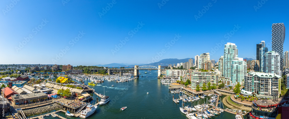 Fototapeta premium Panoramic Aerial View of Granville Island in False Creek with modern city skyline and mountains in background. Downtown Vancouver, British Columbia, Canada.