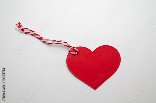 Red Christmas card in the shape of a heart, with a string, on a white surface. Christmas and Christmas greetings.