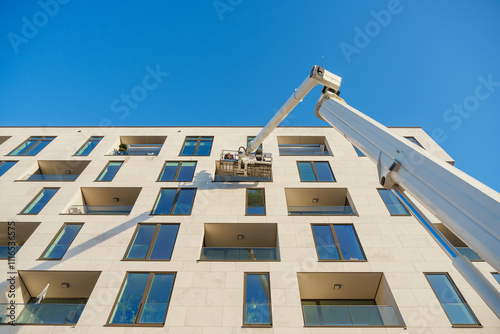 Cleaner worker using a cherry picker to clean a glas facade of a contemporary residential building