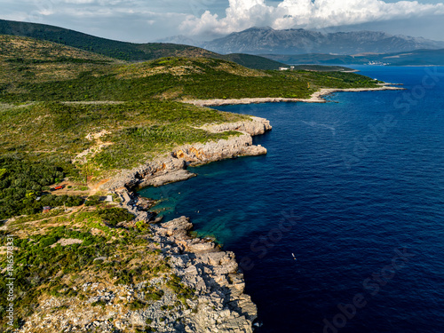 Obraz na płótnie Aerial View of Rocky Shore and Blue Adriatic Water with Mountains and Clouds in the Background w salonie