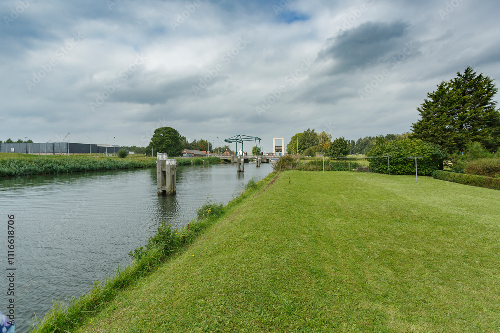 Fototapeta premium Scenic view of a tranquil canal surrounded by lush greenery and cloudy skies in a rural area