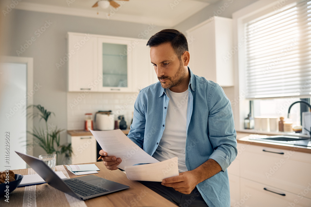 Mid adult man planning home budget while analyzing financial reports at home.