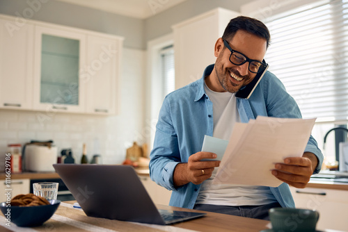 Happy entrepreneur talking on cell phone while analyzing business reports at home. photo