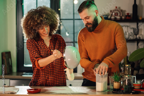 Couple making dough in cozy kitchen, pouring flour and mixing ingredients photo