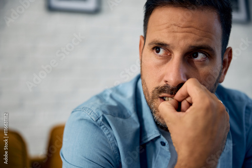 Nervous man biting his fingernails while thinking of something at home. photo