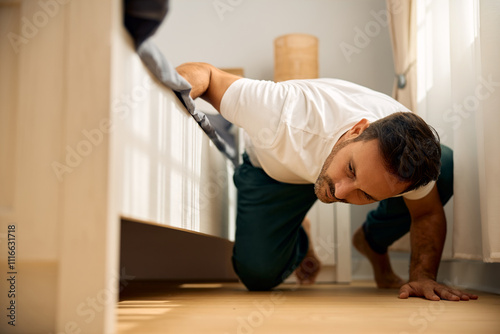 Canvas-taulu Mid adult man searching for something below his bed.