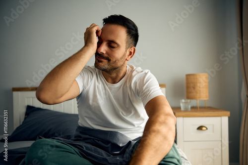 Sleepy man rubbing his eyes after waking up in bedroom.