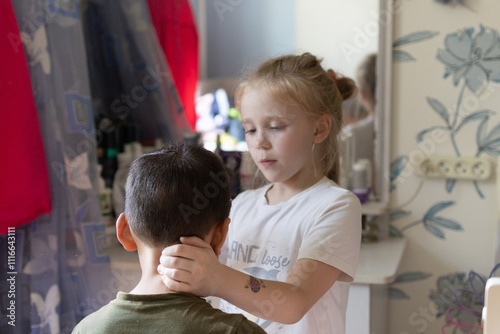 A cute funny girl is playing with a boy friend, combing her hair, a little baby girl is holding a comb, pretending to be a hairdresser, doing her hair, having fun with a friend, chatting at home photo