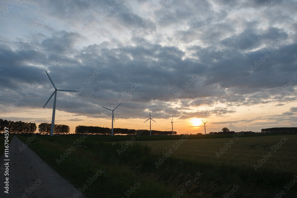 Obraz premium Wind turbines under a dramatic sunset sky in a rural landscape showcasing renewable energy