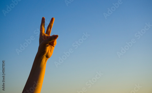 Hand showing number two gesture on blue sea sky background. Gesturing number 2 index finger. Making number two in sign language. Hand counting two. Space for ad text photo