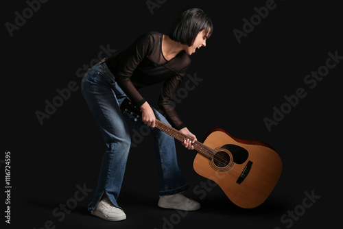 Young woman smashing guitar on black background