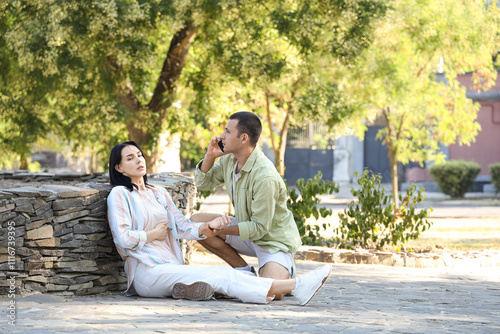 Young man calling ambulance for woman having heart attack in park