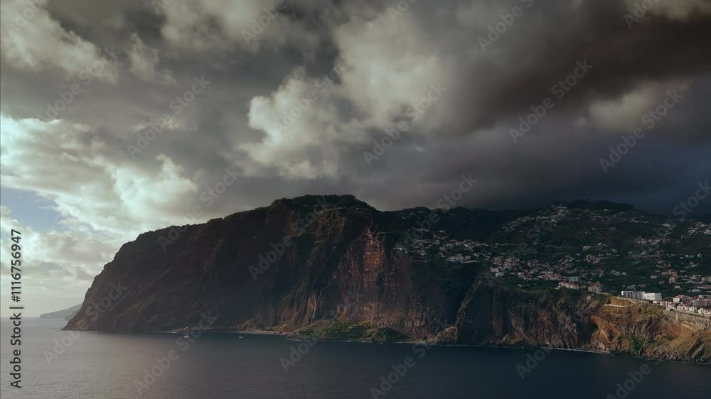A panoramic view of a coastal city by the ocean before a storm, with dramatic clouds, Câmara de Lobos, Madeira.