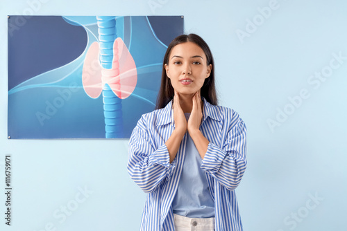 Young Asian woman self-examining thyroid gland near picture on blue background
