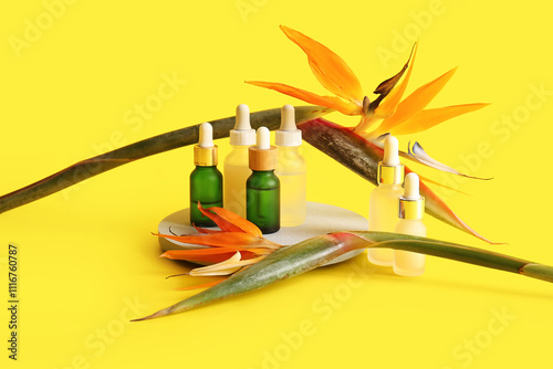 Bottles of cosmetic products and beautiful strelitzia flowers on yellow background photo