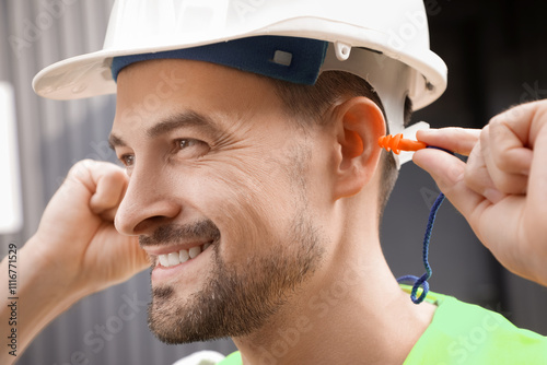 Male builder putting in earplugs outdoors, closeup photo