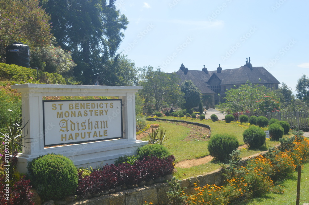 Elegant Sign for St. Benedict Monastery and Happy Vale Amidst Lush Gardens and Stone Buildings Under Blue Sky