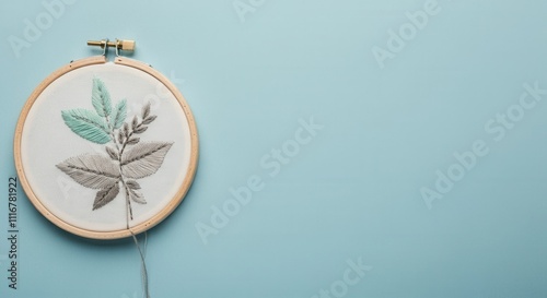 Elegant embroidery hoop with leaf design on light blue background, showcasing intricate needlework, AI photo