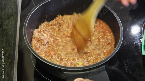 Cooking a savory meat sauce with vegetables and herbs in a kitchen setting