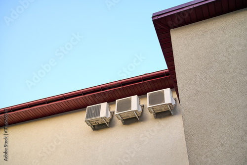 Air conditioning units on the wall of a house. Three air conditioning units are attached to the wall of a house under the roofHigh quality photo