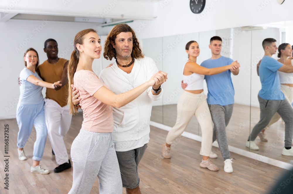 Group of diverse happy adult people dancing modern social dances in pairs at fitness studio Group of diverse happy adult people dancing modern social dances in pairs at fitness studio