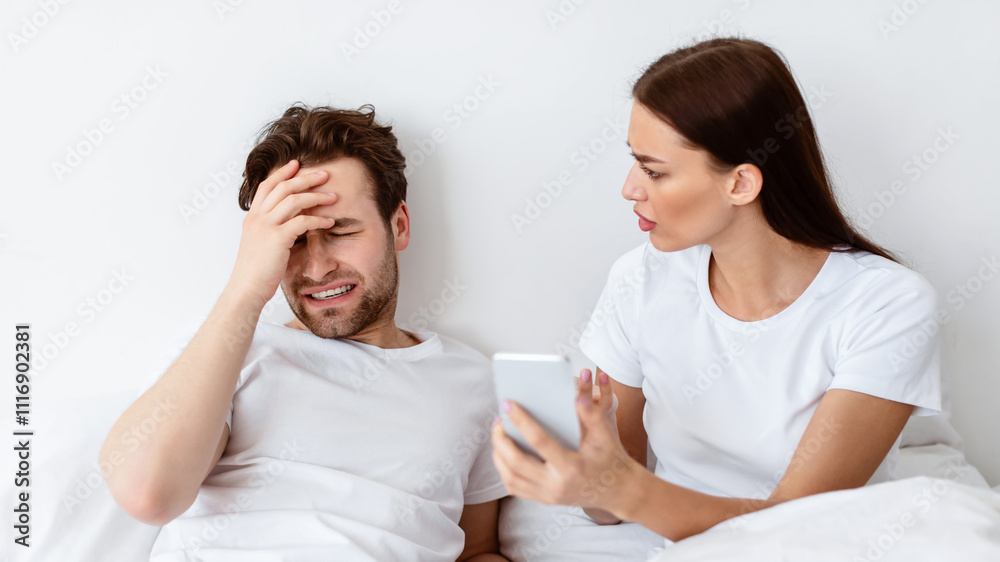 Jealous Wife Showing Cheating Husband His Phone With Message From Lover Demanding Explanation Suspecting Affair Sitting In Bedroom Indoor. Marital Issues, Jealousy In Relationship. Selective Focus Jealous Wife Showing Cheating Husband His Phone With Message From Lover Demanding Explanation Suspecting Affair Sitting In Bedroom Indoor. Marital Issues, Jealousy In Relationship. Selective Focus