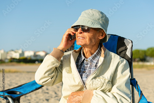 Senior man sitting at the beach, talking on the phone, looking away photo