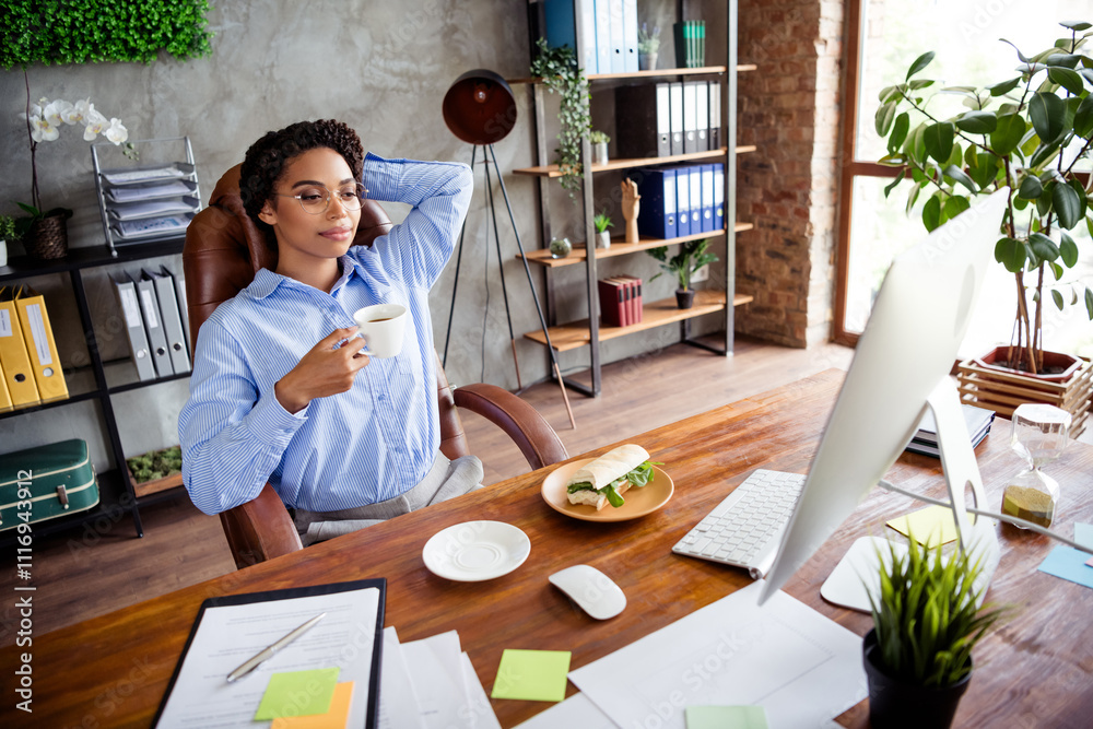 Fototapeta premium Confident young businesswoman enjoys a coffee break in a stylish office setting with elegant decor