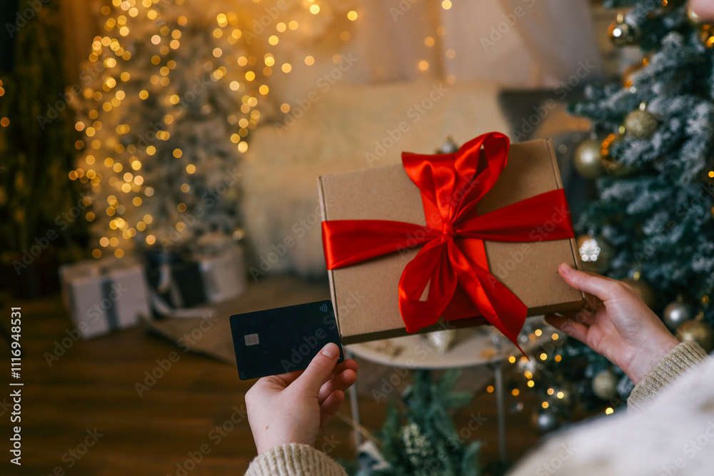 A woman holding a gift box with red ribbon and a credit card, shopping online using a laptop, with a glowing Christmas tree in the background, creating a festive and cozy atmosphere A woman holding a gift box with red ribbon and a credit card, shopping online using a laptop, with a glowing Christmas tree in the background, creating a festive and cozy atmosphere