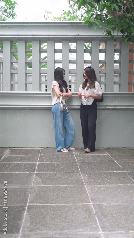 two asian women talking while leaning on the wall two asian women talking while leaning on the wall