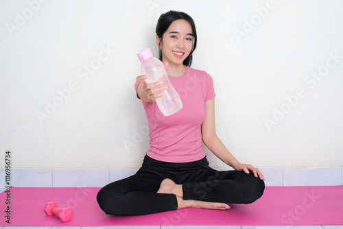 A woman sitting on yoga mat smiling happy while holding a drinking bottle photo