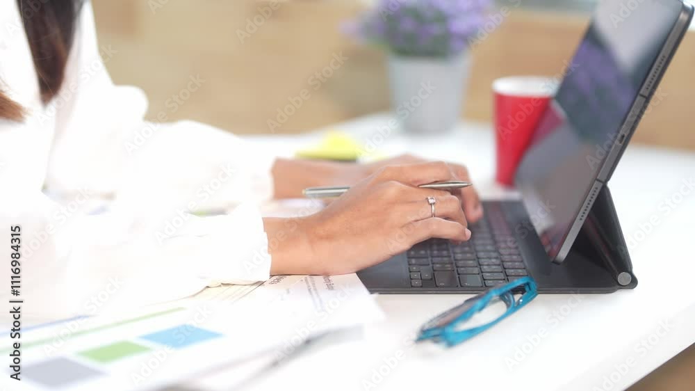A woman is typing on a laptop in front of a potted plant. She is wearing a white shirt and a ring on her finger. Concept of productivity and focus
