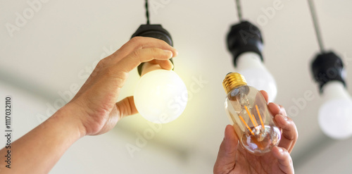 Power saving concept. Hands holding new Light Emitting Diode ( LED ) light bulb with light on and blur spiral compact-fluorescent (CFL) bulbs behind for copyspace.