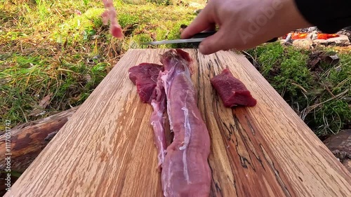 man cutting meat on cutting board in forest