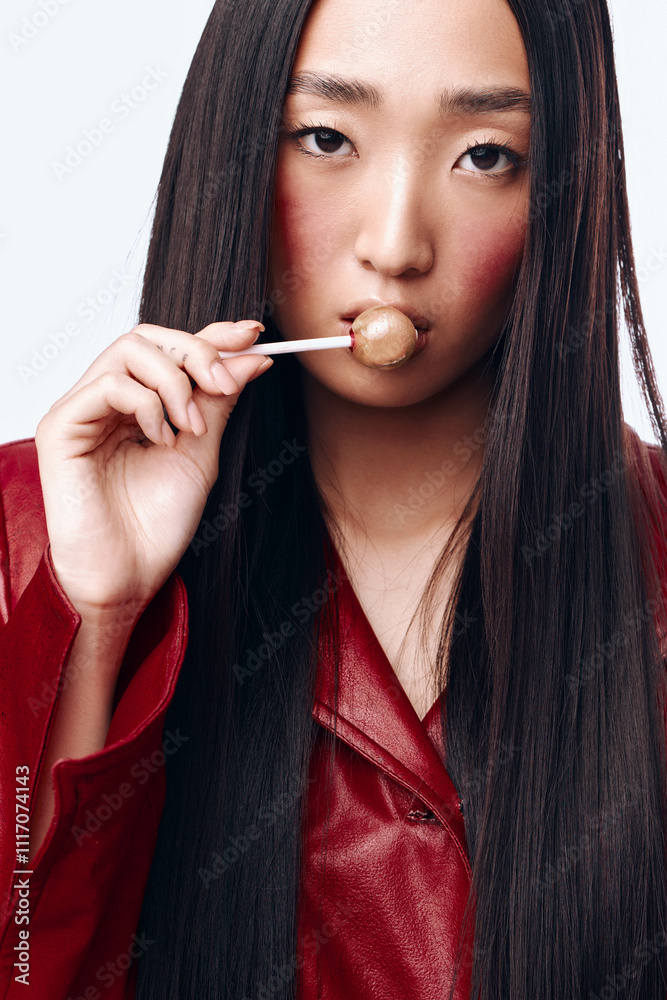 Portrait of a stylish young woman with long black hair and a red jacket playfully holding a stick in her mouth Portrait of a stylish young woman with long black hair and a red jacket playfully holding a stick in her mouth
