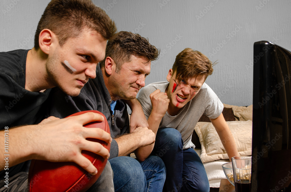 Φωτογραφία Caucasian family of three , father and two sons watching American football on TV