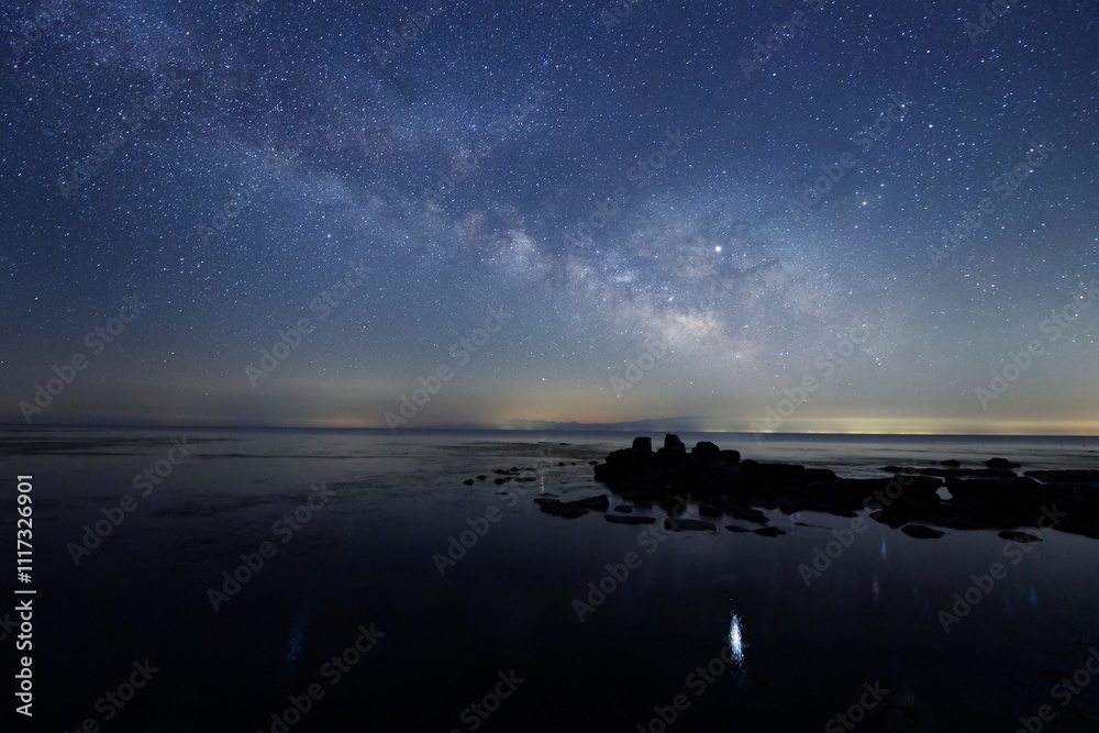 海の水面にゆれる星と天の川と能登半島の星空