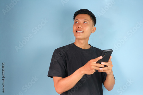 Young Asian man thinking about something while holding his mobile phone