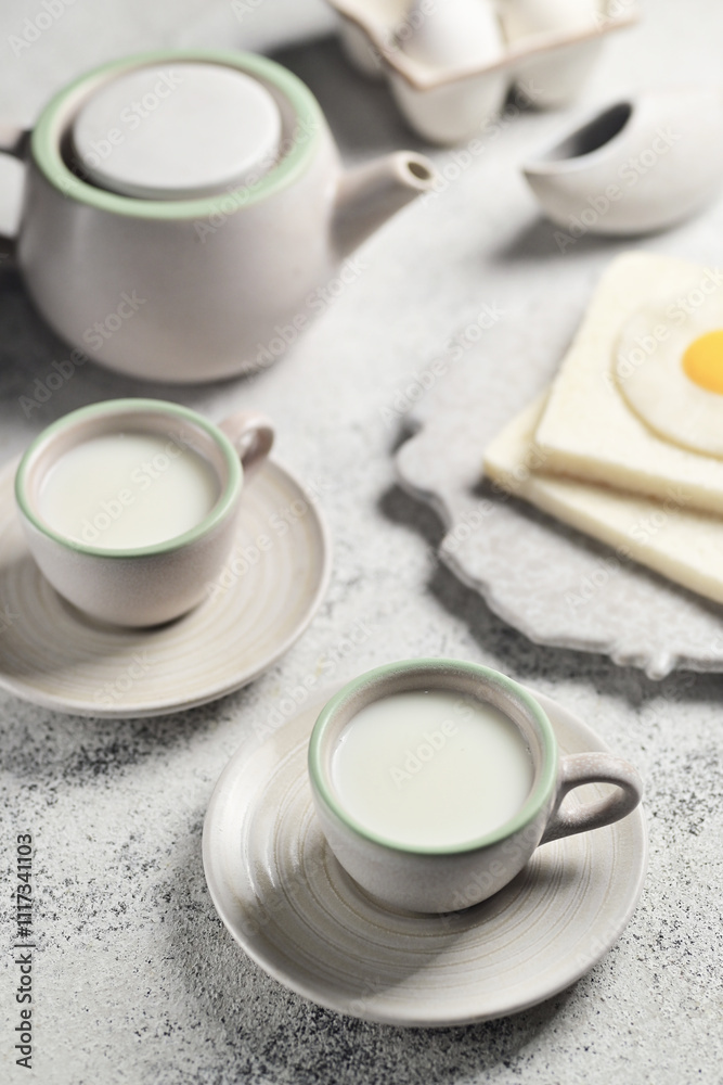 Two cups of white milk accompanied with a teapot and two slices of white bread placed on a wooden board Two cups of white milk accompanied with a teapot and two slices of white bread placed on a wooden board