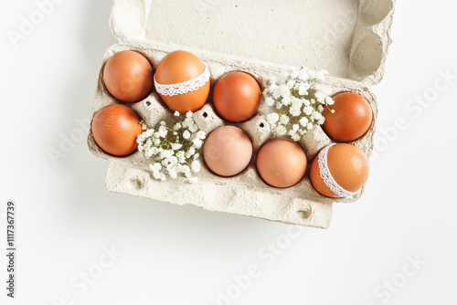 Brown Easter eggs decorated lace and white gypsophila flowers in carton on white background. Easter celebration concept. Top view photo of festive food of dyed chicken egg, minimal style, copyspace photo