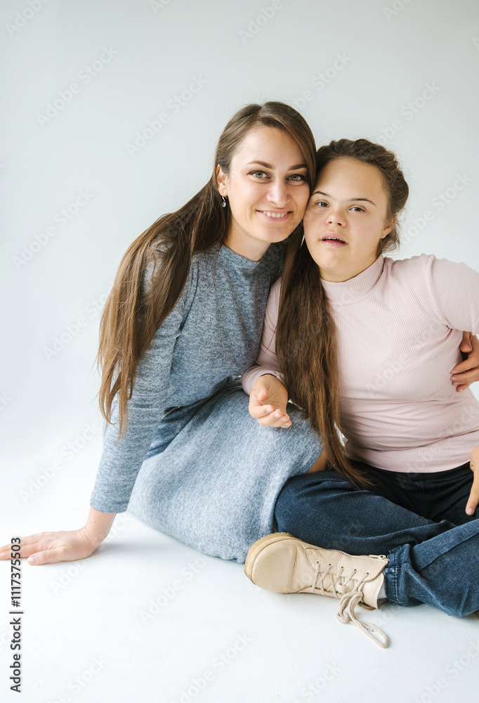 A cheerful mother and daughter with Down syndrome sit together on a white background, their happy smiles and close embrace radiating warmth and love A cheerful mother and daughter with Down syndrome sit together on a white background, their happy smiles and close embrace radiating warmth and love