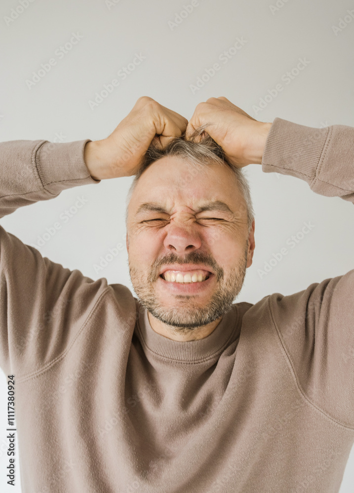 Obraz premium Close-up portrait of a man clutching his hair in frustration or anger. His face is contorted in a grimace, eyes squeezed shut, expressing intense negative emotion. 